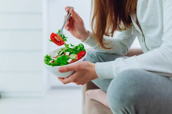 Healthy woman in sportswear holding a bowl of fresh vegetable salad at home. Balanced organic diet and clean fitness eating.