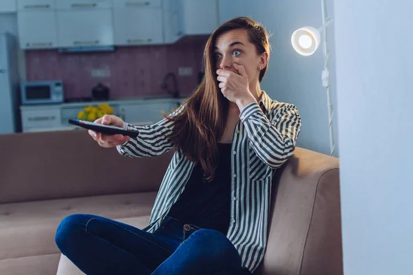 Shocked, frightened woman watching a horror movie at home alone