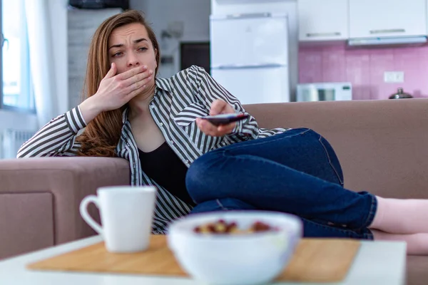 stock image Woman resting on the couch and yawning while watching TV alone at home 