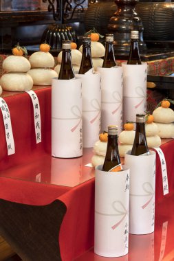 tokyo, japan - january 07 2019: tokyo, japan - january 07 2019: bottles of sake rice liquor placed as offerings in front of kagami mochi rice ball topped with a clementine for New Year's celebrations in Tokyo's Gokokuin temple.