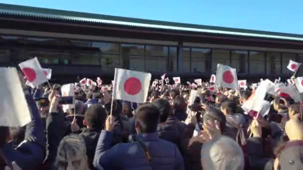 皇居長和殿のバルコニーに天皇皇后両陛下の姿が映像で映し出され、旗を振る来場者を出迎える。. — ストック動画