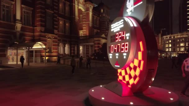 Video van de officiële olympische tijdwaarnemer Omega countdown klok voor de Olympische en Paralympische Spelen Tokio 2020 voor het station van Tokio 's nachts. — Stockvideo