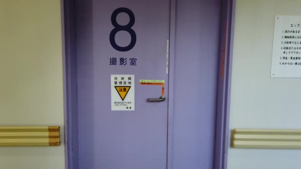 Вниз, чтобы вверх наклон видео японской больницы Токио в отделении радиологии IRM, чьи двери отображают слова "X-RAY ROOM" и "Осторожно" — стоковое видео