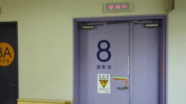 Right to left pan video of an empty corridor of a Japanese hospital of Tokyo in the IRM radiology department whose doors display the words 'Changing rooms', 'MRI radiology room' 