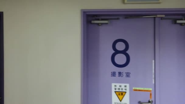 Walking video in an empty corridor of a Japanese hospital of Tokyo in the IRM radiology department whose doors display the words 'Changing rooms', 'MRI radiology room' — Wideo stockowe