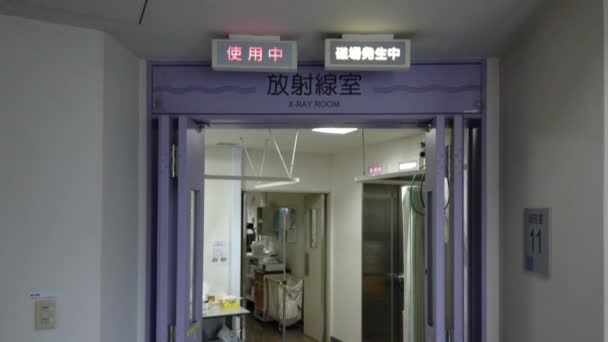 Vídeo inclinado hacia abajo de un hospital japonés de Tokio en el departamento de radiología del IRM cuya puerta muestra las palabras 'Sala de Rayos X', 'MRI' y en letras brillantes 'En uso' — Vídeos de Stock