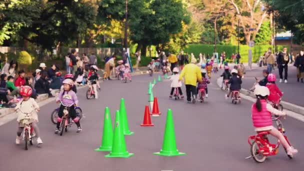 Video statico di alcuni genitori giapponesi che vegliano sui bambini che indossano caschi praticando biciclette su biciclette da allenamento a Tokyo . — Video Stock