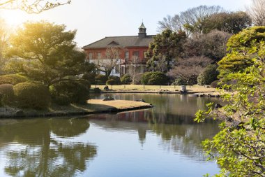 Tokyo, Japonya - 20 Mart 2020: Koishikawa Botanik Bahçeleri 'nin Japon bahçesinin gölünde arka planda Üniversite Müzesi' nin Koishikawa Ek Binası 'nın kırmızı tuğlalı köşkü var..