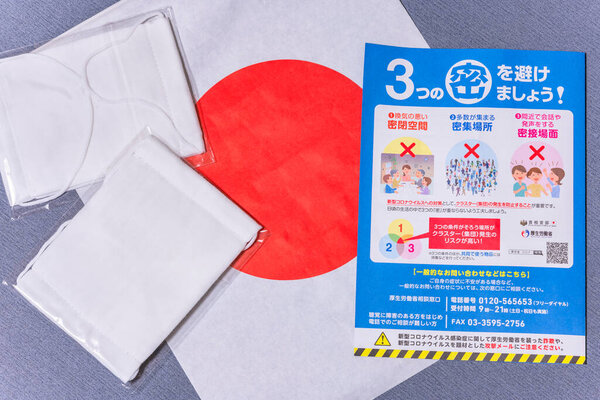 tokyo, japan - may 20 2020: Cloth masks and leaflet promoting social distancing sent by Japanese govt to cope with the chronic shortage and fight the spread of coronavirus (COVID-19) on a Japan flag.