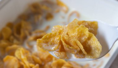 Kahvaltılık gevrek. Kızarmış altın mısır taneleri beyaz kaşıkta sütle