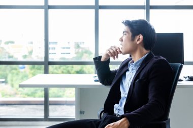 Genç Asyalı işadamı modern bir ofiste oturuyor ve iş performansını artırmak için çözümler bulmaya çalışıyor..