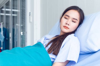 Asyalı genç bayan hastalar mavi gömlekler giyip parlak yüzlü yatakta yatıyorlar. Doktorun kontrol etmesini beklerken daha iyi semptomlar gösteriyorlar.