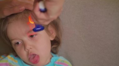 Ateşin yüksek olduğunu gösteren dijital kızılötesi termometreyle hasta palyaço çocuğun ateşini ölçüyor. Surat asan küçük kızın ateşi yüksek. Salgın, grip salgını konsepti. Yetişkin kızın ateşi kontrol ediliyor. Soğuk, yeni yürümeye başlayan