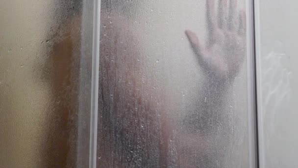 Muž se koupe ve sprše, zpomaluje, voda teče tělem, mokrý chlap, voda teče zamrzlým sklem — Stock video