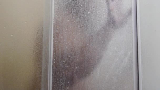 Un homme se baigne dans une douche, au ralenti, l'eau coule à travers le corps, mec humide, l'eau coule à travers le verre givré — Video