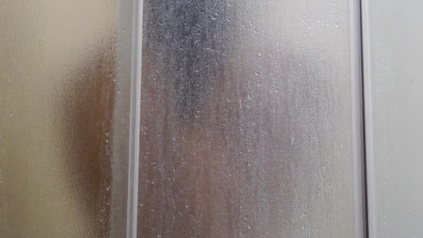 Un hombre se baña en una ducha, cámara lenta, el agua corre a través del cuerpo, chico mojado, el agua fluye a través del vidrio esmerilado — Vídeos de Stock