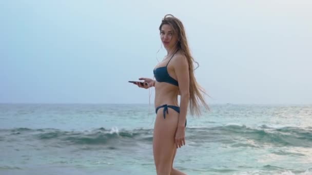 Sports women on the beach of Sri lanka walks in the ocean, long hair, rejoices, listens to music — Stock Video