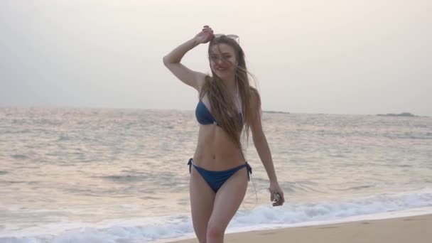 Стройная девушка с длинными волосами гуляет по океану, танцует, слушает музыку — стоковое видео