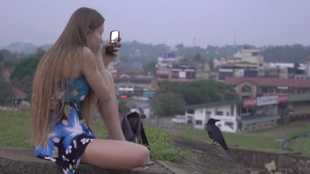 Kvinna med långt hår, blond, i klänning, sitter på gräset och gör make-up själv — Stockvideo