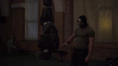 Gümüş kafatası maskeli manyak, siyah bir çanta taşıyan kurbanını muayene ediyor.