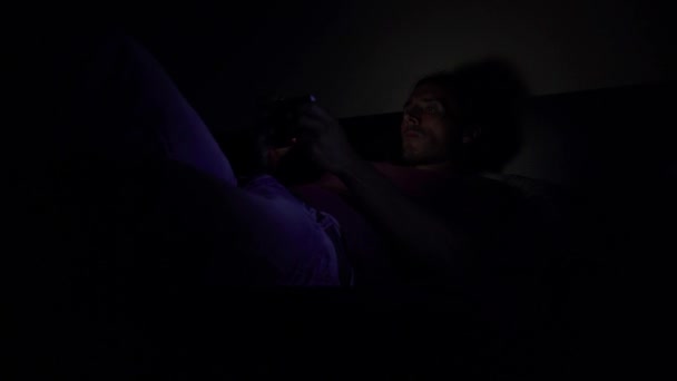 The guy is lying on the bed in a dark room and looking at the phone — Stock Video