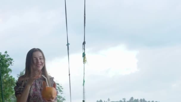 Une femme sur l'océan monte sur une balançoire, boit du lait de coco, ralentit — Video