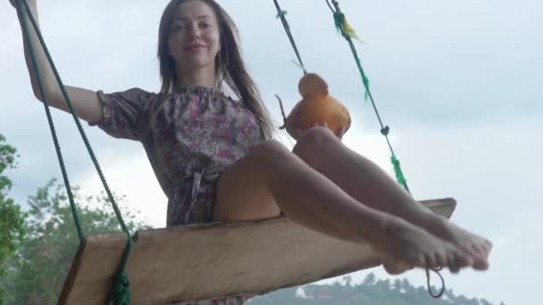 Een meisje op de oceaan rijdt op een schommel, drinkt kokosmelk — Stockvideo