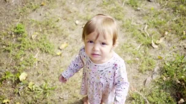 En liten flicka går på gräset, i en vit klänning med blommor, sommar på en solig dag — Stockvideo