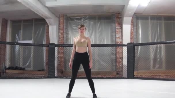 Mulher fina e bonita, de calças pretas e top bege, faz um aquecimento antes de treinar no octógono — Vídeo de Stock