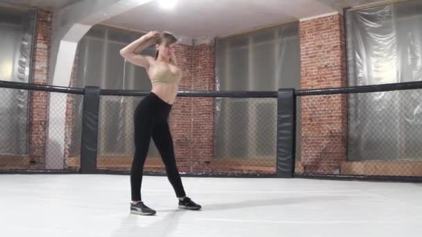 Piękna sexy dziewczyna, w czarnych spodniach i beżowy top, robi rozgrzewkę przed treningiem w ośmiokącie — Wideo stockowe