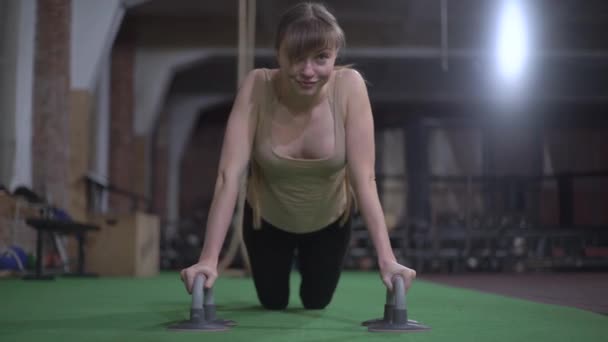 Mooie vrouw, met lang blond haar, traint, doet push-ups, kijkt naar de camera en glimlacht — Stockvideo