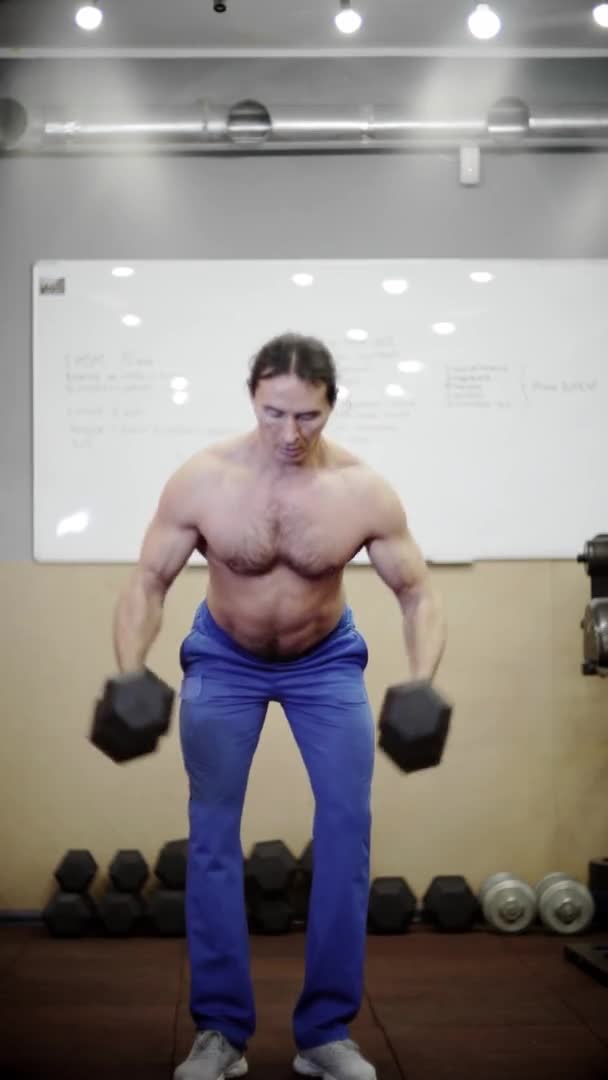 Hombre atlético hace ejercicios con mancuernas, trenes hombros, video vertical — Vídeos de Stock