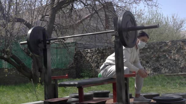 Sportler trainiert im Garten seines Hauses, während der Quarantäne in Selbstisolierung, macht eine Langhantelpresse aus der Brust — Stockvideo