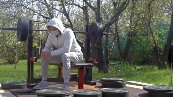 Молодий чоловік, в захисній масці, під час карантину відпочиває в саду свого будинку — стокове відео