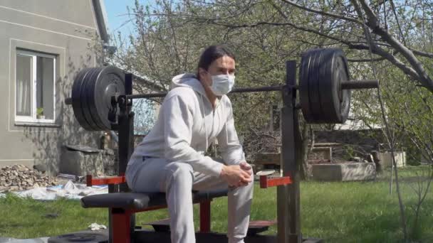 Een jonge man, met een beschermend masker, tijdens quarantaine rust na traning in de tuin — Stockvideo