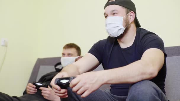 Két férfi álarcban a koronavírus járvány alatt, nevetnek és szórakoznak, videojátékokat játszanak otthon. — Stock videók