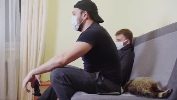 Két férfi álarcban a koronavírus járvány alatt, nevetnek és szórakoznak, videojátékokat játszanak otthon. — Stock videók