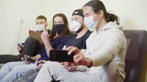 Four men in protective masks during the epidemic of coronavirus rest laugh and fun, Guys take selfies, show fuck you in camera, playing video games — Wideo stockowe