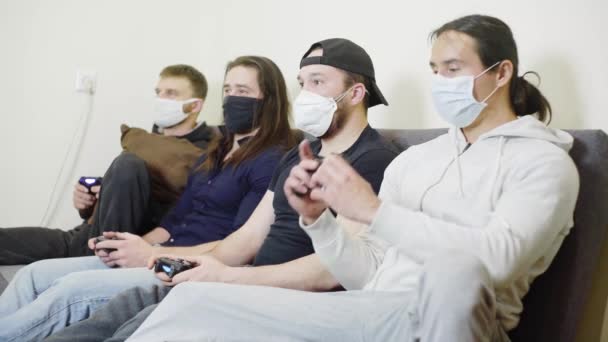 Quatro caras durante a epidemia de coronavírus resto rir divertido, em máscaras de proteção jogando videogames em casa — Vídeo de Stock