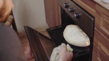 Bir adam mutfakta yemek pişirir, fırında peynir ve otlarla turta pişirir.