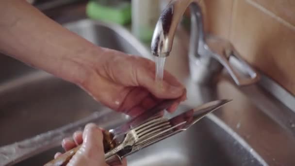 En man rengör köket, tvättar knivar och gafflar över diskhon — Stockvideo