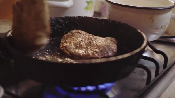 Bir adam mutfakta bir tavada biftek pişiriyor, et pişirişini izliyor. — Stok video