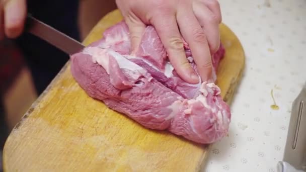 Ο τύπος κόβει ωμό κρέας σε μια ξύλινη σανίδα, μαγειρεύει μπριζόλα στην κουζίνα. — Αρχείο Βίντεο