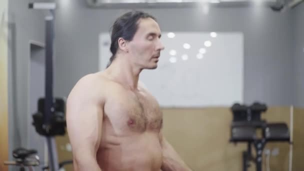 Een man met een naakte romp, mooie spieren, doet een warming-up in de sportschool, voor de training, strekt zijn armen uit — Stockvideo