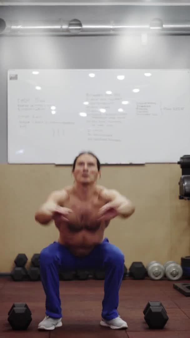 Un hombre con un hermoso torso, realiza sentadillas y saltos, Marco de video vertical 9: 16 — Vídeo de stock