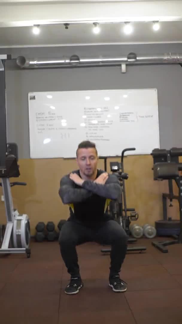 Ein gutaussehender Typ im schwarzen Trainingsanzug erklärt dem Publikum, wie man Kniebeugen macht, vertikales Video — Stockvideo