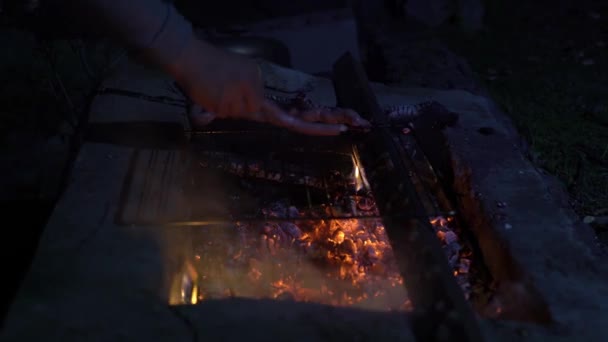 Чоловік смажить сосиски на вогні, вночі на подвір'ї — стокове відео