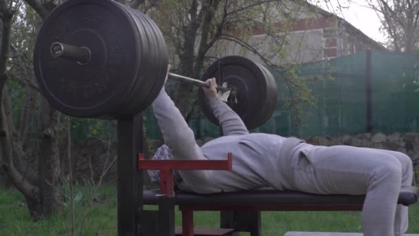 Een man traint op de binnenplaats van het huis, tijdens quarantaine, op zelfisolatie, verhoogt de lat — Stockvideo