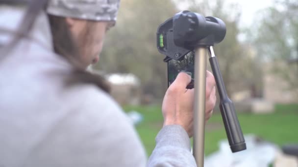 El tipo prepara el teléfono para la filmación de vídeo, un teléfono inteligente en un trípode — Vídeos de Stock