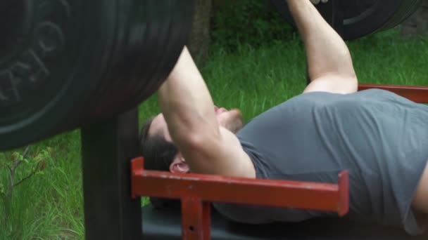 Atleta hombre entrena en el jardín de su casa, durante la cuarentena en auto-aislamiento, hace un prensa de la barra desde el pecho — Vídeo de stock